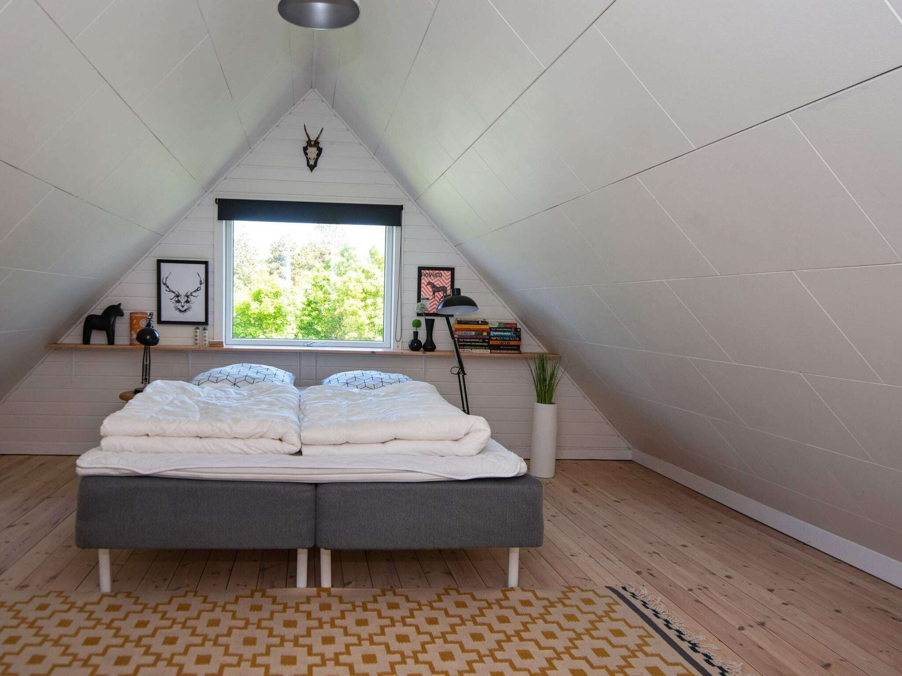 A bedroom with a loft bed, a window with a view of trees, a shelf with books and a lamp, and a decorative skull on the wall.