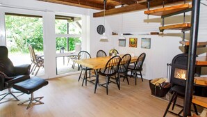 Un espace repas comprenant une table et des chaises en bois, une cheminée et une vue sur la verdure environnante.