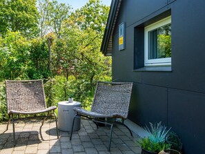 Une terrasse avec deux fauteuils en osier, une table ronde et une plante en pot.
