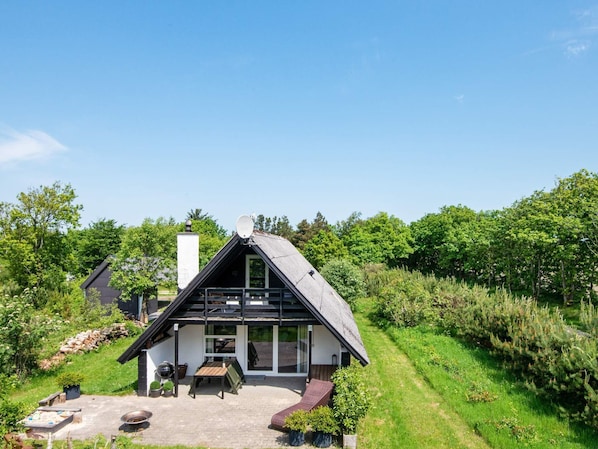 A modern house with a sloped roof, a patio with outdoor furniture, and a garden.