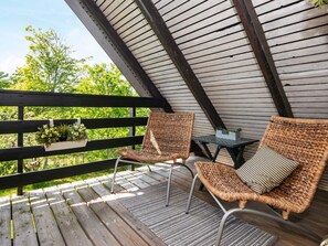 A wooden deck with two wicker chairs and a small table, overlooking a lush green landscape.