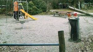 Un parque infantil con tobogán y estructuras para escalar, rodeado de árboles y bancos.