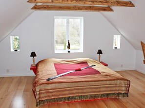A bedroom with a sloped ceiling, a bed with a patterned bedspread, two bedside lamps, and a window with a view of greenery. - Holiday Home in Söderåkra (Soderakra)