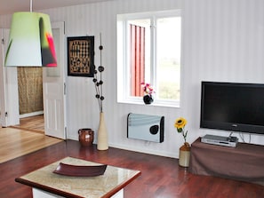 A living room with a flat-screen TV, a coffee table, a vase with a sunflower, and a window with curtains. - Holiday Home in Söderåkra (Soderakra)