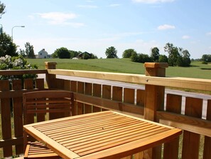 A wooden deck with a table and chairs, overlooking a grassy field with trees and a building in the distance. - Holiday Home in Söderåkra (Soderakra)