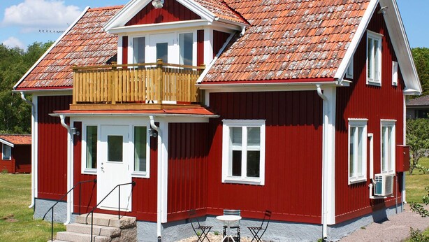 A red two-story house with a balcony, a chimney, and a small front porch with a table and chairs.