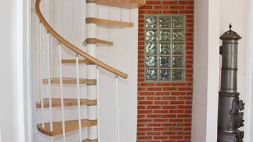A spiral staircase with wooden steps and white railings, a brick wall with a decorative window, and a tall, ornate metal object.