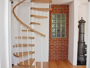 A spiral staircase with wooden steps and white railings, a brick wall with a decorative window, and a tall, ornate metal object.