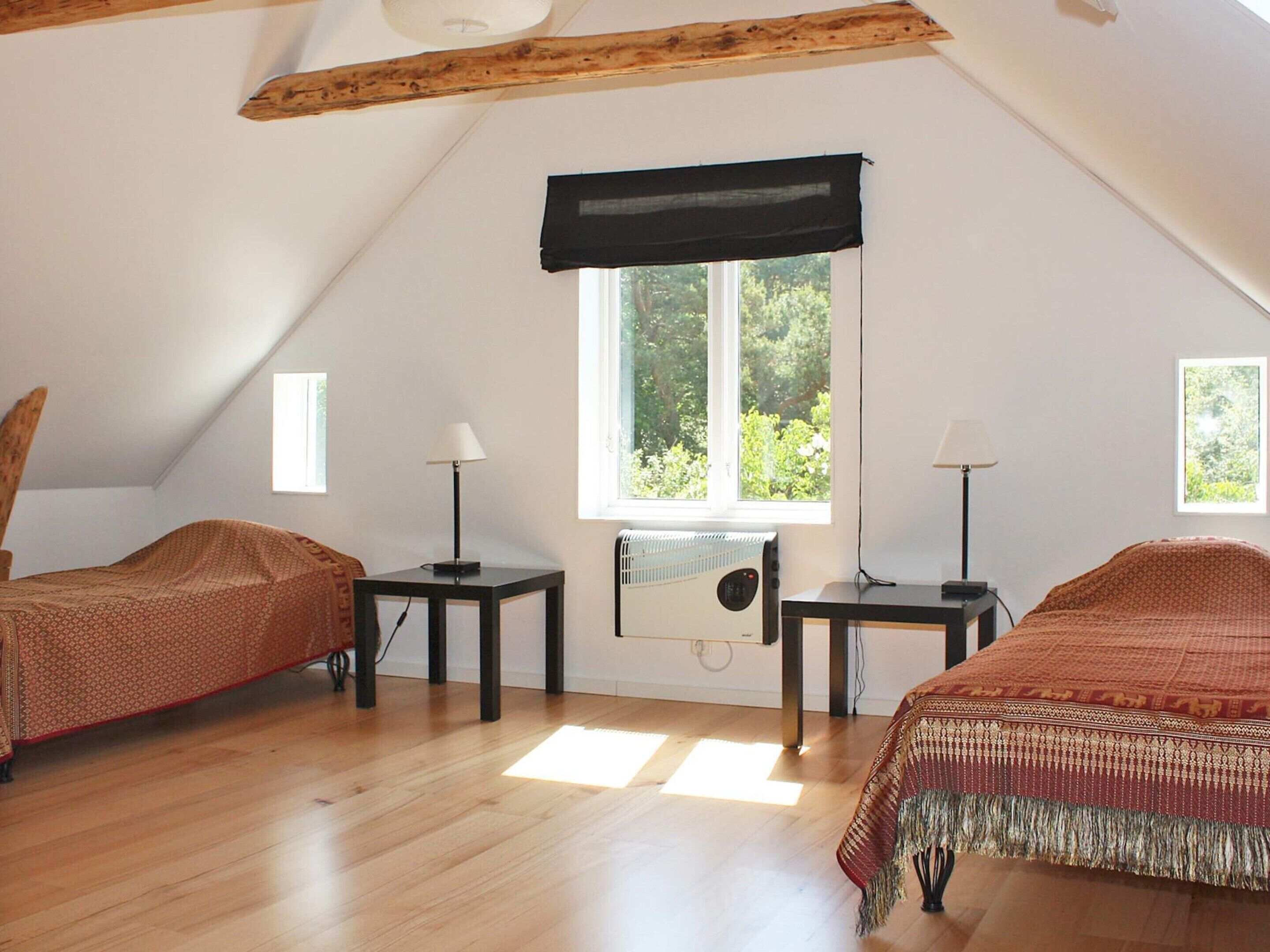 Una habitación con dos camas, una ventana, un radiador y una viga en el techo.