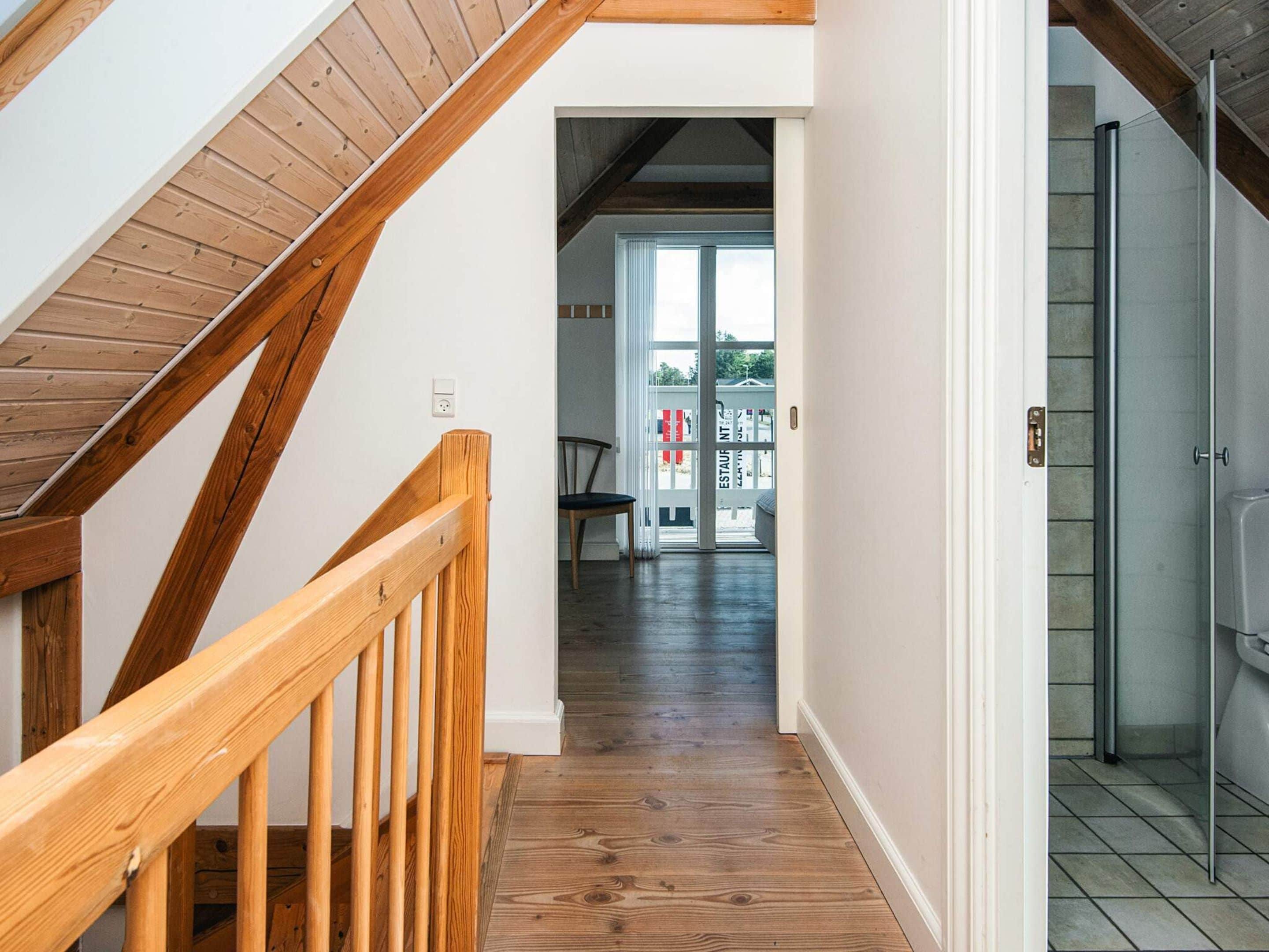 A wooden staircase leading to a room with a glass shower and a view of an outdoor area with a sign.