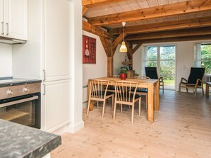 A kitchen with white cabinets and a wooden ceiling, a dining area with a table and chairs, and large windows. - 4 Star Holiday Home in Blavand (Blavand)