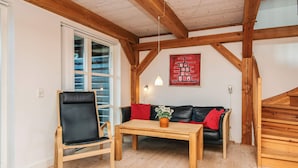 A room with a wooden ceiling, a black leather chair, a wooden table, a black sofa with red cushions, and a wooden staircase. - 4 Star Holiday Home in Blavand (Blavand)