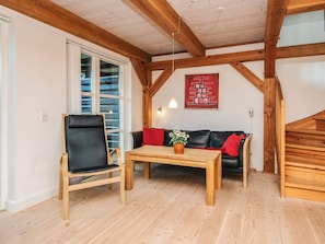A room with a wooden ceiling, a black leather chair, a wooden table, a black sofa with red cushions, and a wooden staircase. - 4 Star Holiday Home in Blavand (Blavand)