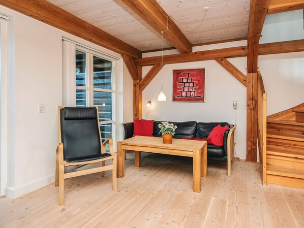 A room with a wooden ceiling, a black leather chair, a wooden table, a black sofa with red cushions, and a wooden staircase. - 4 Star Holiday Home in Blavand (Blavand)