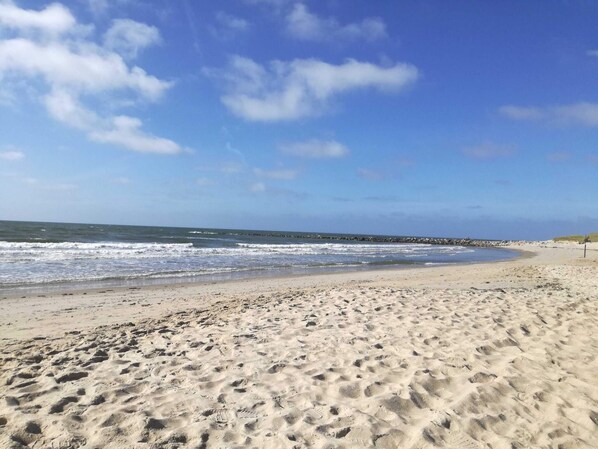 A sandy beach with waves, a clear sky, and a rocky outcrop in the distance. - 4 Star Holiday Home in Blavand (Blavand)