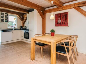 A modern kitchen with white cabinets, a wooden dining table with four chairs, and a red abstract painting on the wall. - 4 Star Holiday Home in Blavand (Blavand)