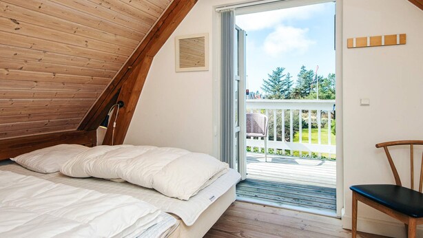 Une chambre avec un lit, une chaise et un balcon donnant sur un paysage verdoyant.
