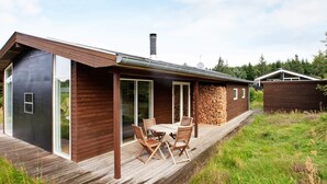 A modern house with a wooden deck, a dining area with chairs, and a stack of firewood. - Eco-friendly Retreat in Nature - By Traum Ferienwohnungen (Fjerritslev)