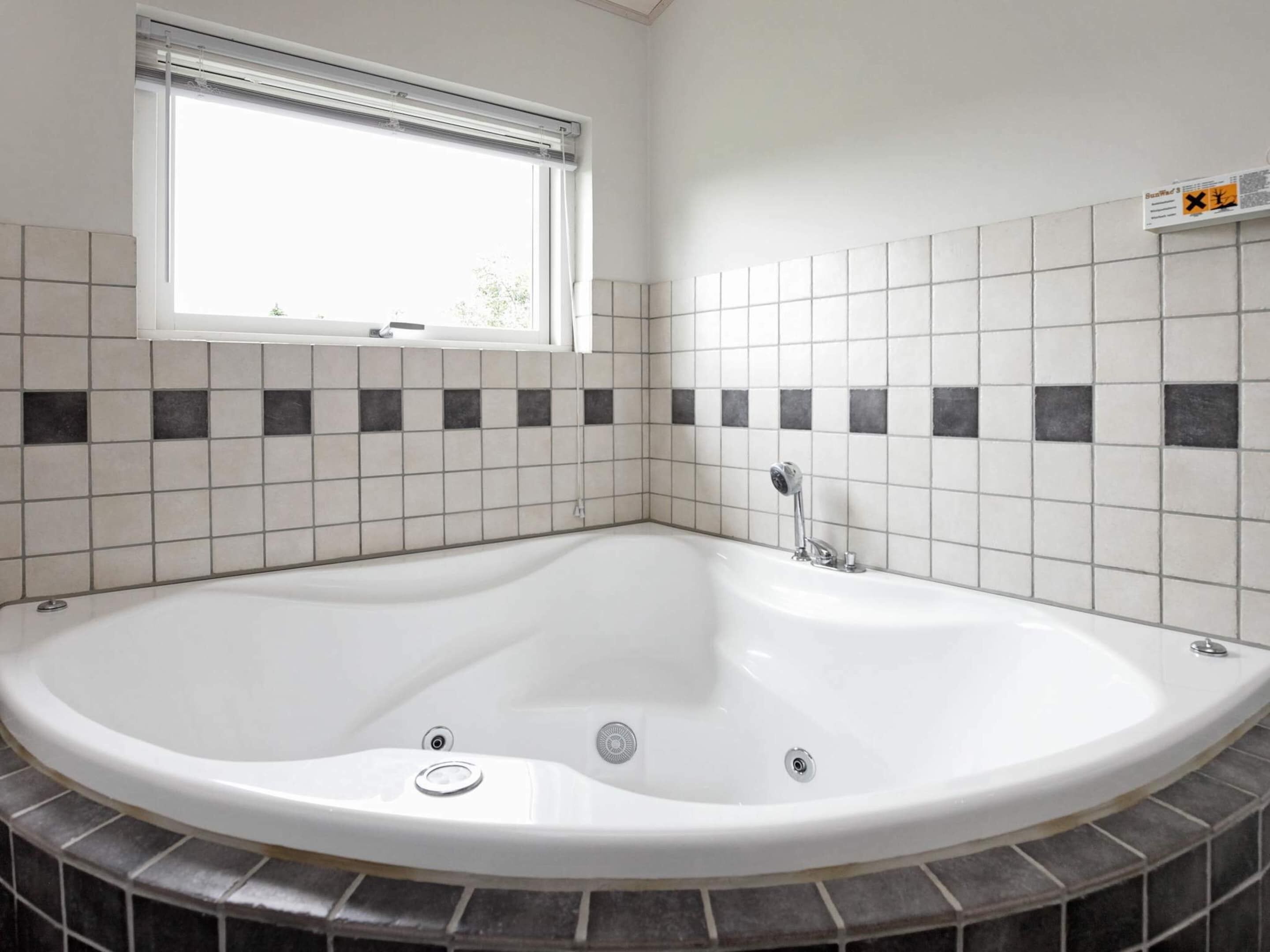 Un baño moderno con una bañera independiente, una ventana y una pared de azulejos con una combinación de blanco y tonos oscuros.