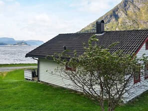 A white building with a dark roof, a small porch, and a view of a body of water and mountains.