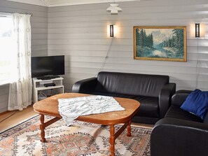 A living room with a sofa, a coffee table, a television, a painting, and a patterned rug.