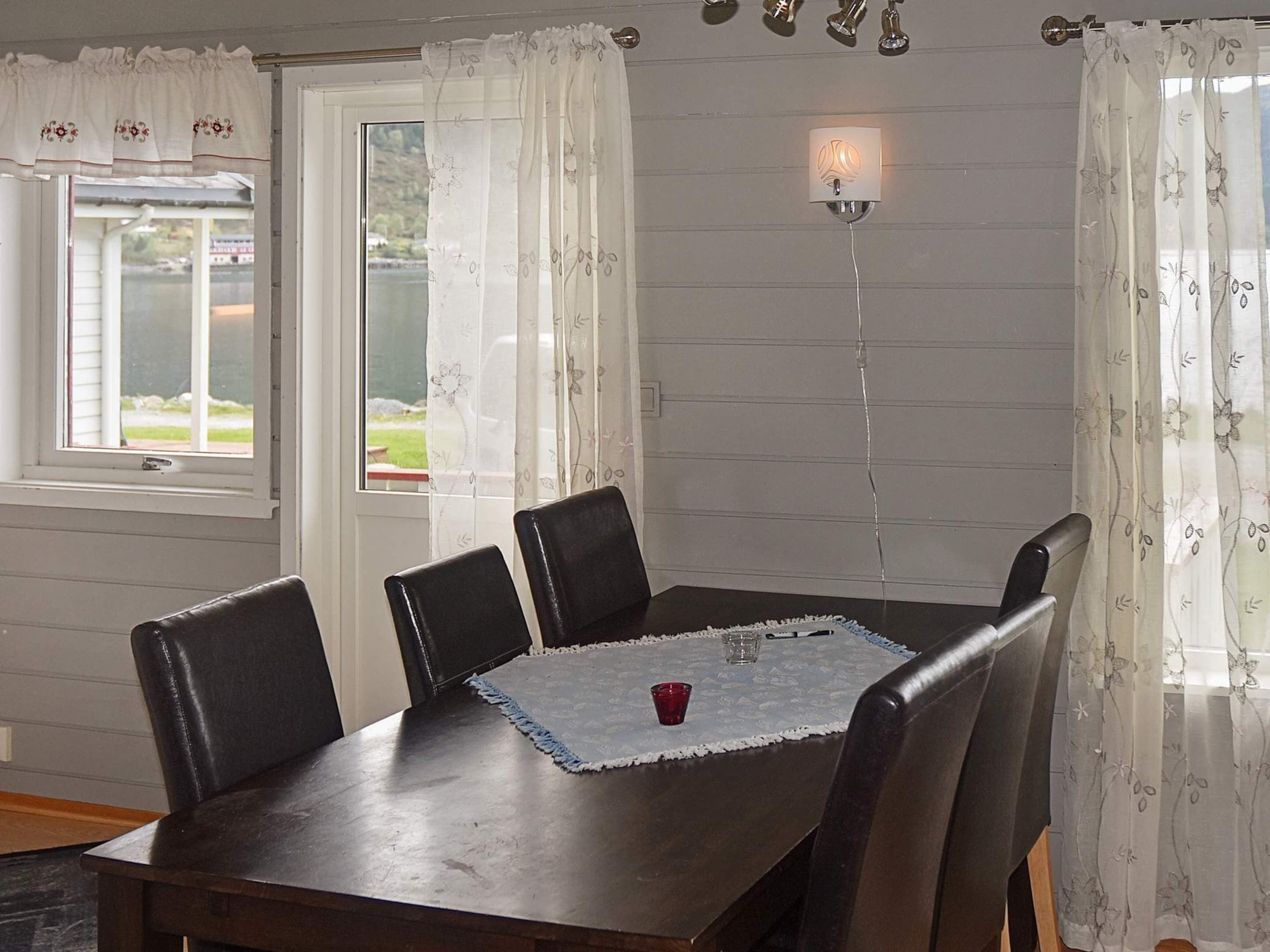 Un coin repas avec une table en bois, quatre chaises, un chemin de table en dentelle et une tasse rouge.