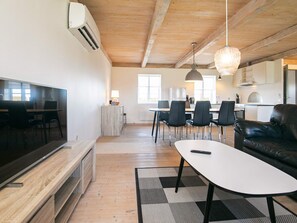 A modern living room with a flat-screen TV, a leather sofa, a dining area with chairs, and a kitchen in the background. - Contemporary Apartment in Faaborg near Sea (Faaborg)