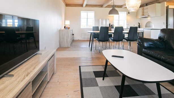 A modern living room with a flat-screen TV, a leather sofa, a dining area with chairs, and a kitchen in the background. - Contemporary Apartment in Faaborg near Sea (Faaborg)