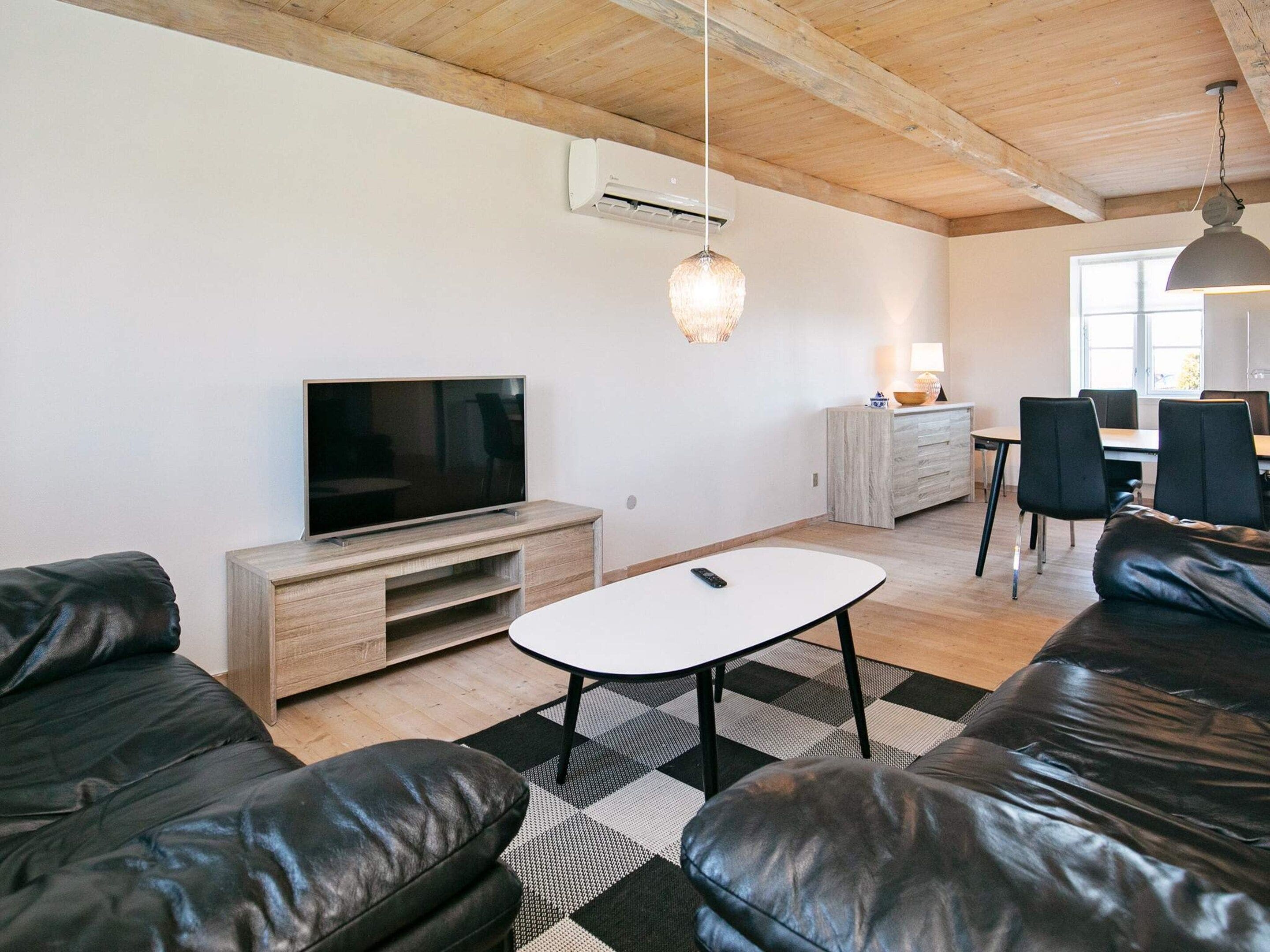 Uma sala de estar moderna com televisão de tela plana, sofás de couro, mesa de centro e um espaço de jantar com cadeiras e mesa.