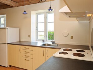 A kitchen with a double sink, a stove, wooden cabinets, and a window with a view of greenery. - Contemporary Apartment in Faaborg near Sea (Faaborg)