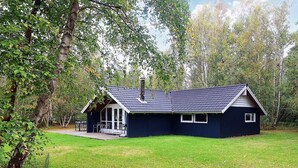 A small, dark-colored cabin with a sloped roof, a chimney, and a glass door entrance. - 9 Person Holiday Home in Vaeggerlose-by Traum (Vaeggerlose)