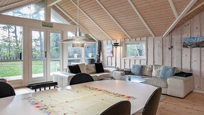 A cozy cabin interior with a dining table, chairs, a sofa, and a large window offering a view of the outdoors. - 9 Person Holiday Home in Vaeggerlose-by Traum (Vaeggerlose)