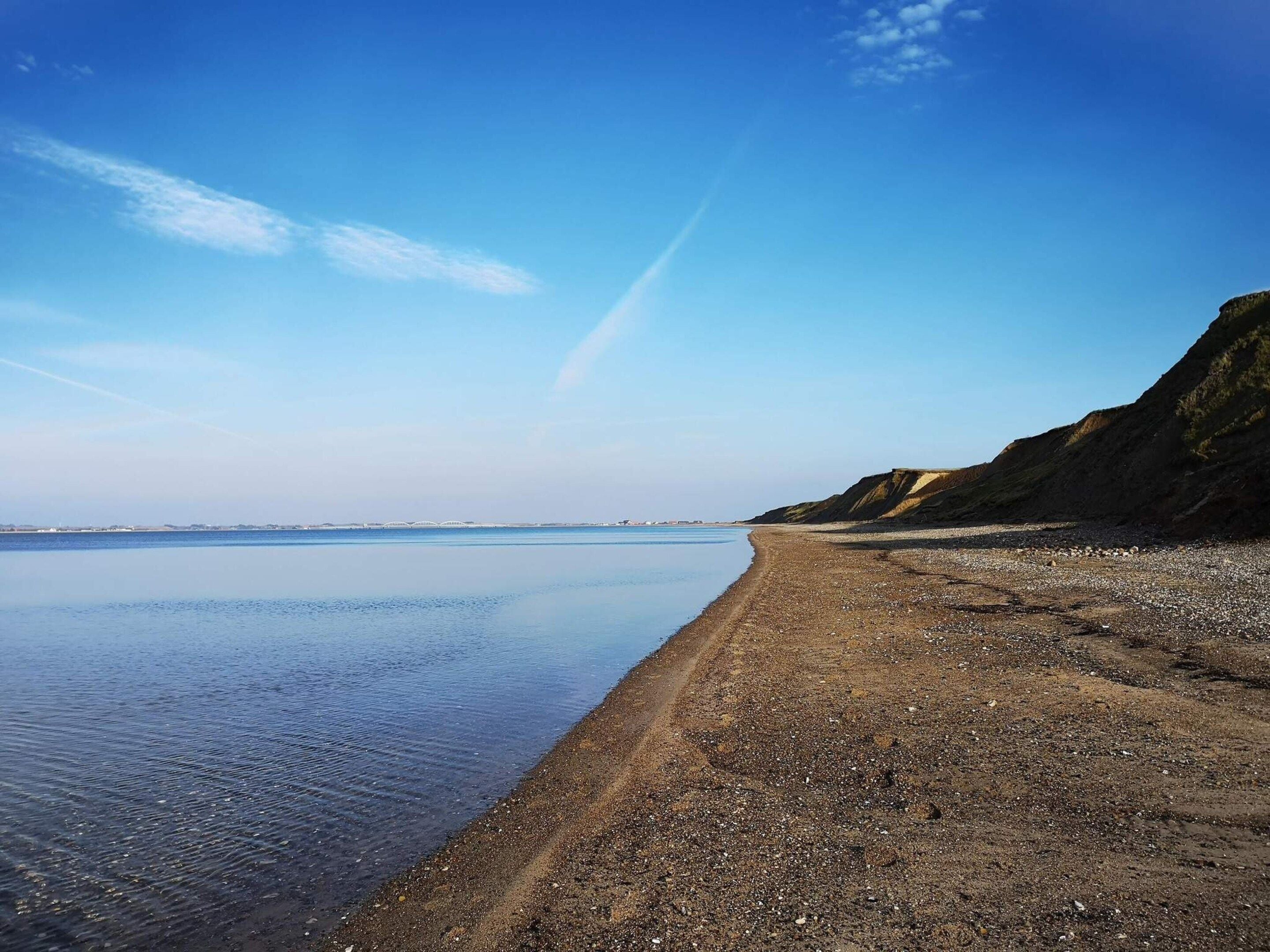 A beach with a clear sky, calm water, and a rocky shoreline.