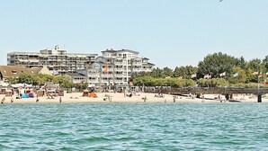 Ett hotell vid kusten med flera våningar, en strand i förgrunden och en klar himmel.