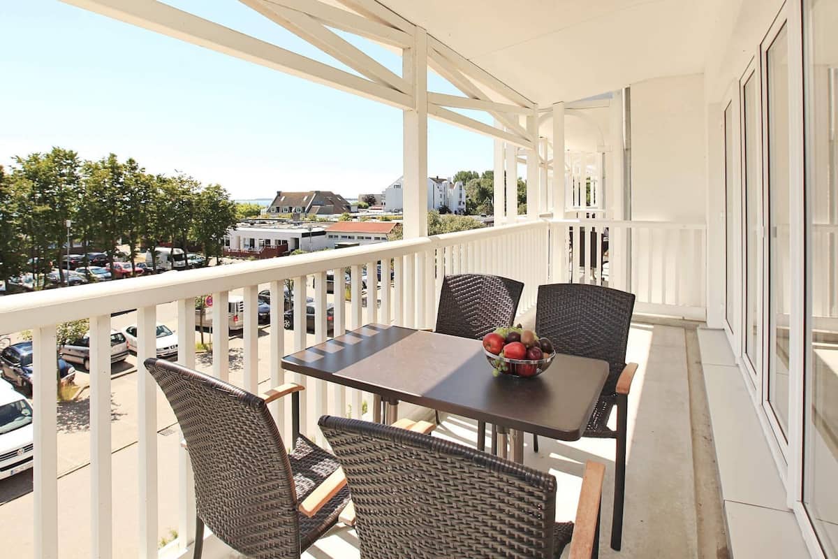 A balcony with a table and chairs, a bowl of fruit, and a view of the street and buildings.