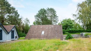 A small, single-story building with a sloped roof, surrounded by a grassy field and trees. - Peaceful Holiday Home in Ebeltoft near Sea (Ebeltoft)