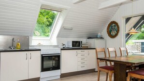 A kitchen with a skylight, a microwave, an oven, and a dining area with wooden chairs and a table. - Peaceful Holiday Home in Ebeltoft near Sea (Ebeltoft)