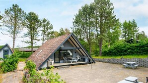 A modern, triangular-roofed cabin with a patio area, surrounded by trees and a stone pathway. - Peaceful Holiday Home in Ebeltoft near Sea (Ebeltoft)