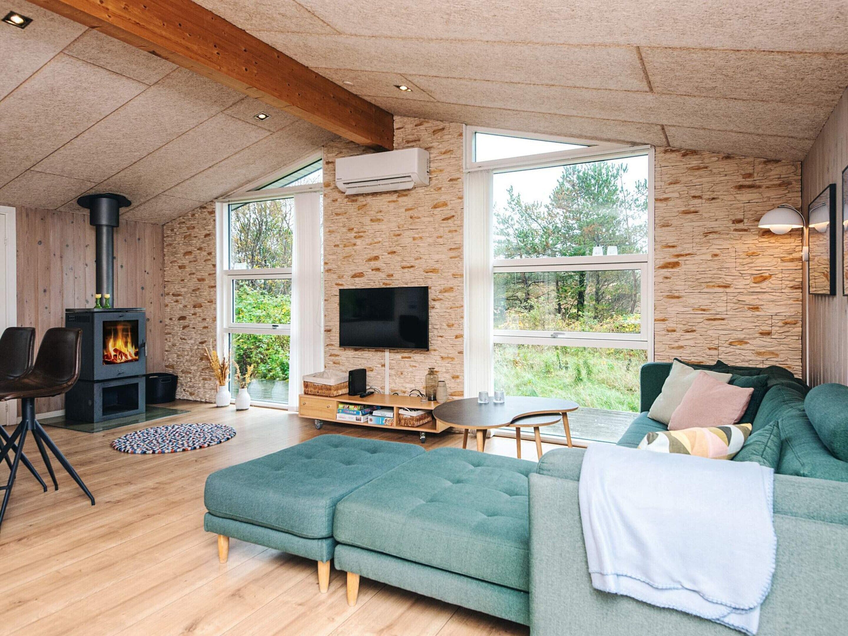 Ein gemütliches Wohnzimmer mit Steinwand, Kamin, Fernseher und großem Fenster mit Blick auf Grünflächen.