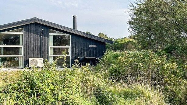 A modern wooden cabin with large windows, a chimney, and a fan outside.