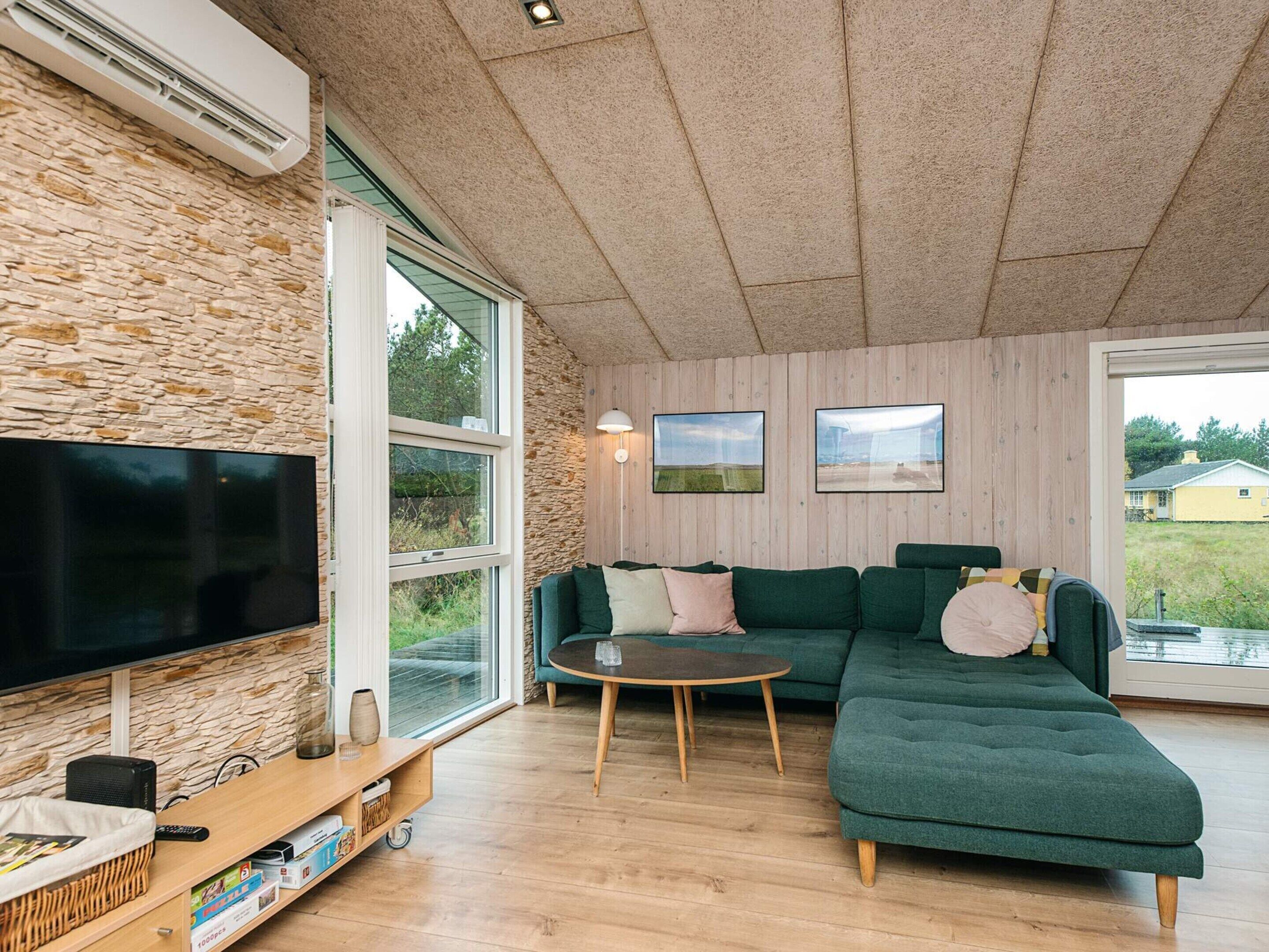 A modern living room with a stone wall, a large flat-screen TV, a green sectional sofa, a round coffee table, and a wooden entertainment unit.