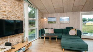 A modern living room with a stone wall, a large flat-screen TV, a green sectional sofa, a round coffee table, and a wooden entertainment unit.