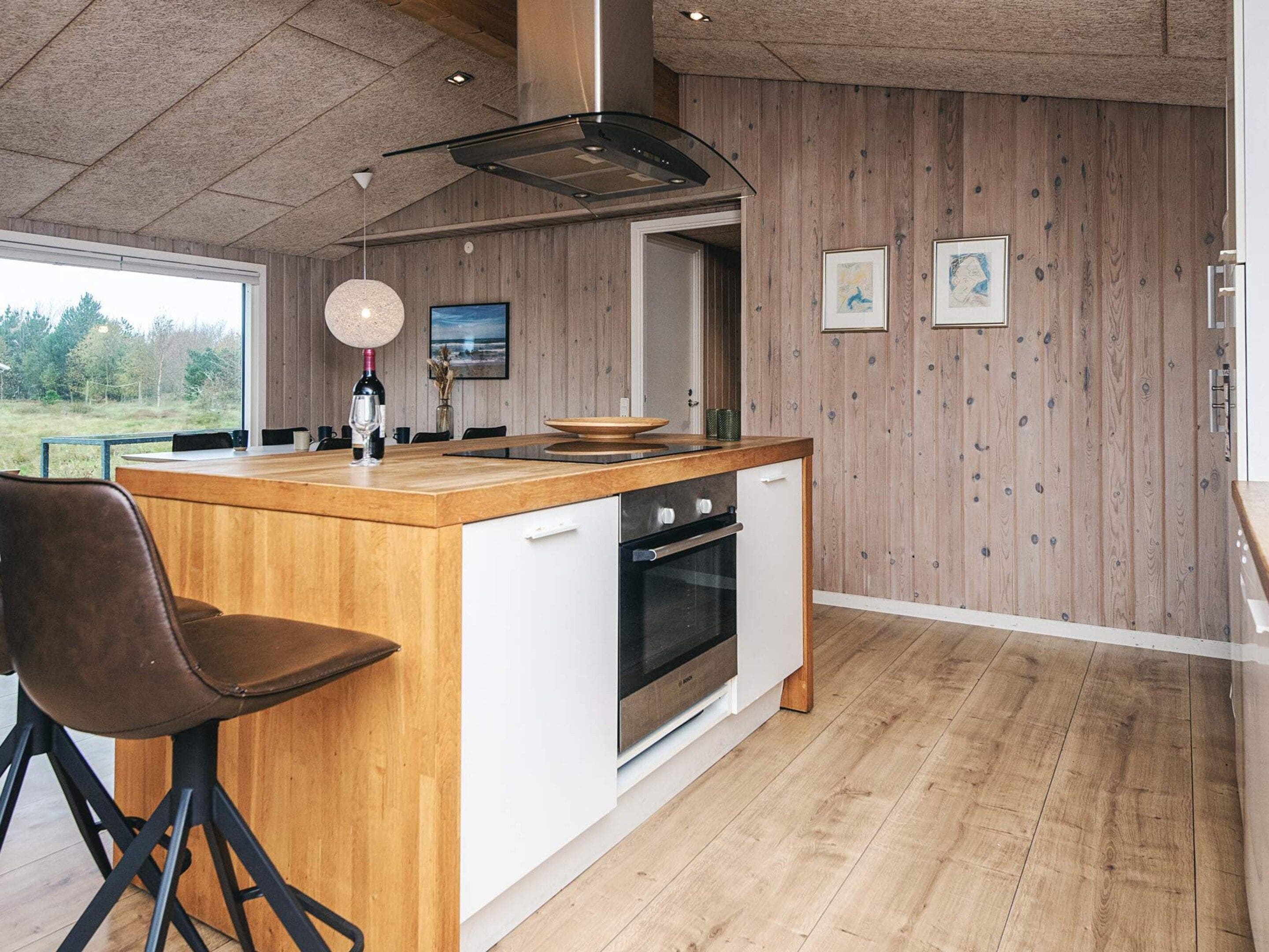 Une cuisine moderne avec un îlot central en bois, des appareils électroménagers blancs et une vue sur l’extérieur.