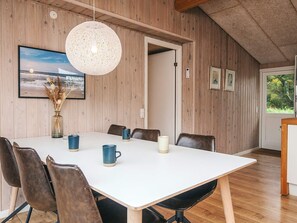 Un comedor con una mesa blanca, sillas de cuero marrón, una lámpara colgante y paredes de madera.