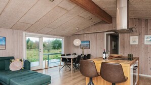 A spacious living area with a green sofa, a wooden dining table with chairs, and a large window offering a view of greenery.