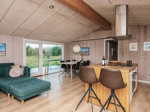 A spacious living area with a green sofa, a wooden dining table with chairs, and a large window offering a view of greenery. - Fabulous Holiday Home in FanÃ¸ near Sea (Fano)