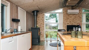 A modern kitchen with a wood stove, white cabinets, and a large window overlooking a garden.