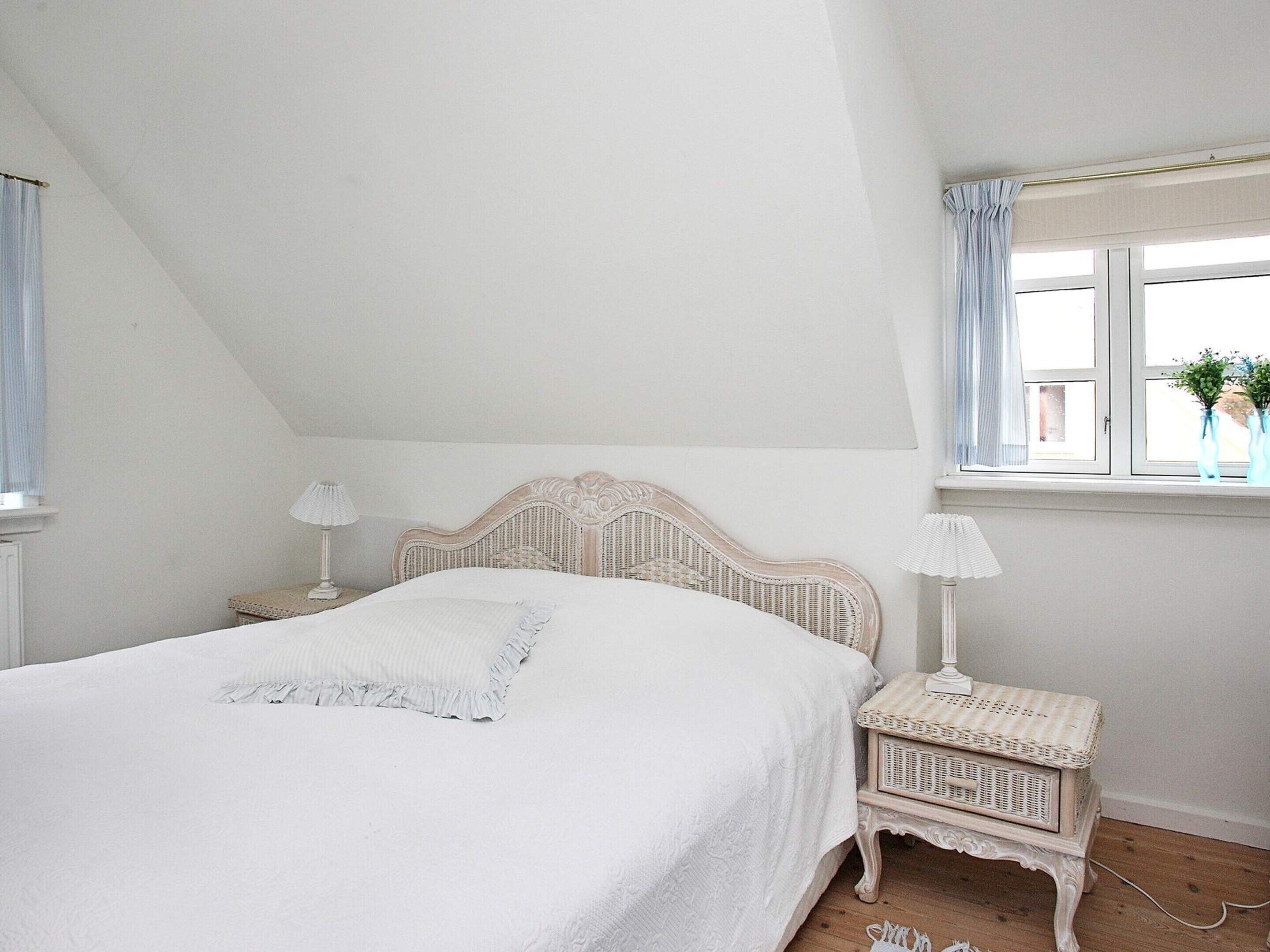 A bedroom with a bed, nightstands, a window with curtains, and a small table by the window.
