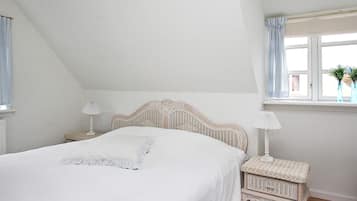 A bedroom with a bed, nightstands, a window with curtains, and a small table by the window.