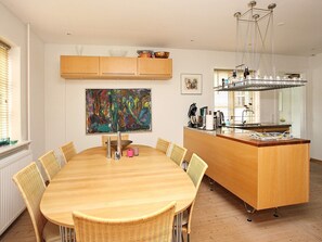 A modern kitchen with a central island, a dining table with chairs, and a large abstract painting on the wall. - 5 Person Holiday Home in Skagen-by Traum (Skagen)